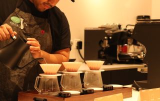 USBrC competitor Andres Morales brewing three pour overs on a counter.